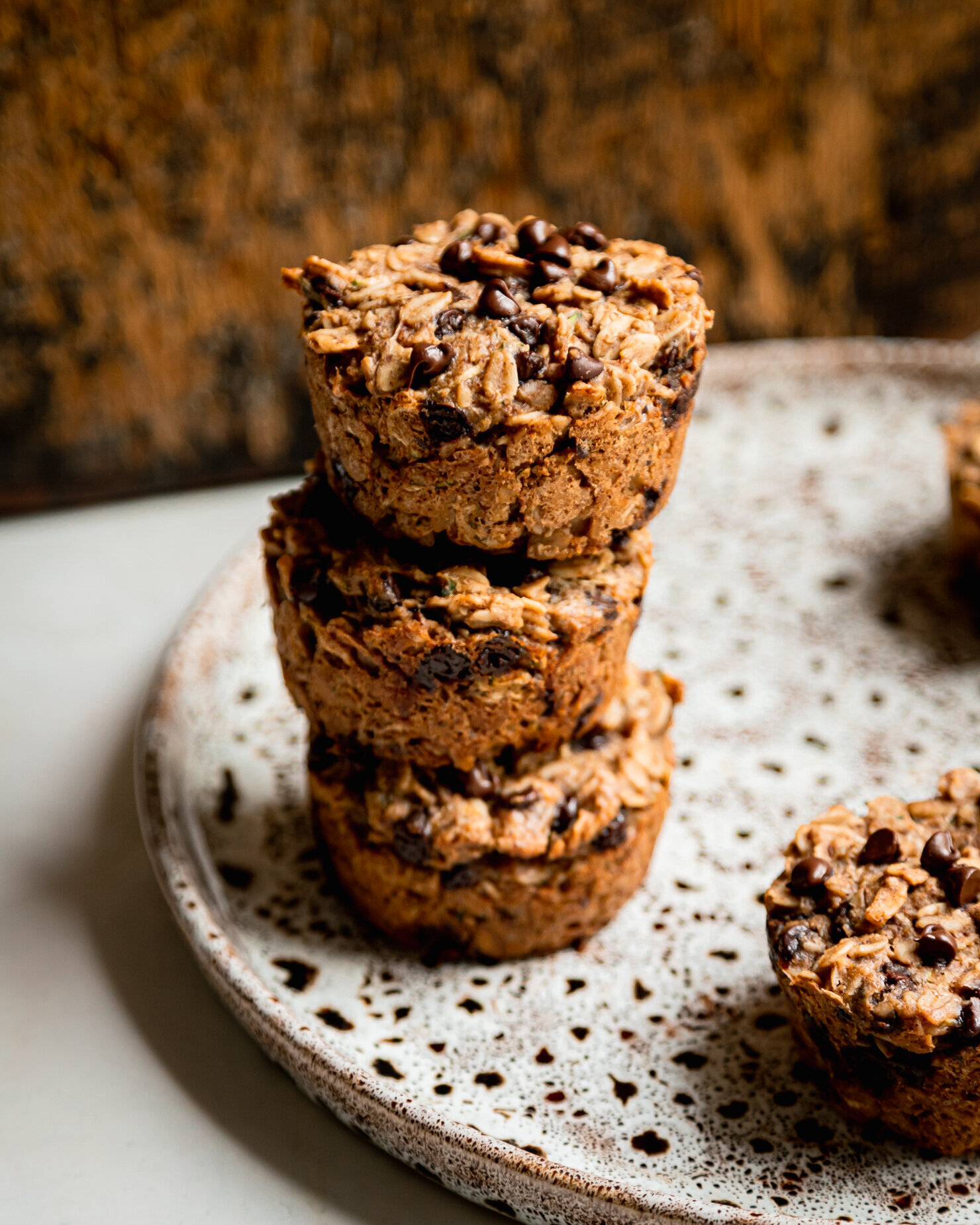 A slight 3/4 angle shot shows 3 baked zucchini oatmeal cups stacked on top of each other. The oatmeal cups have chocolate chips dotted throughout.