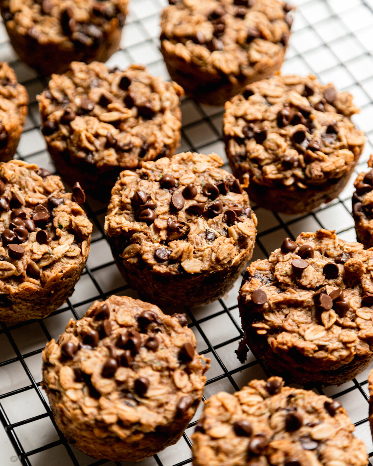 A slight 3/4 angle shows a bunch of baked zucchini oatmeal cups with chocolate chips cooling on a wire rack.
