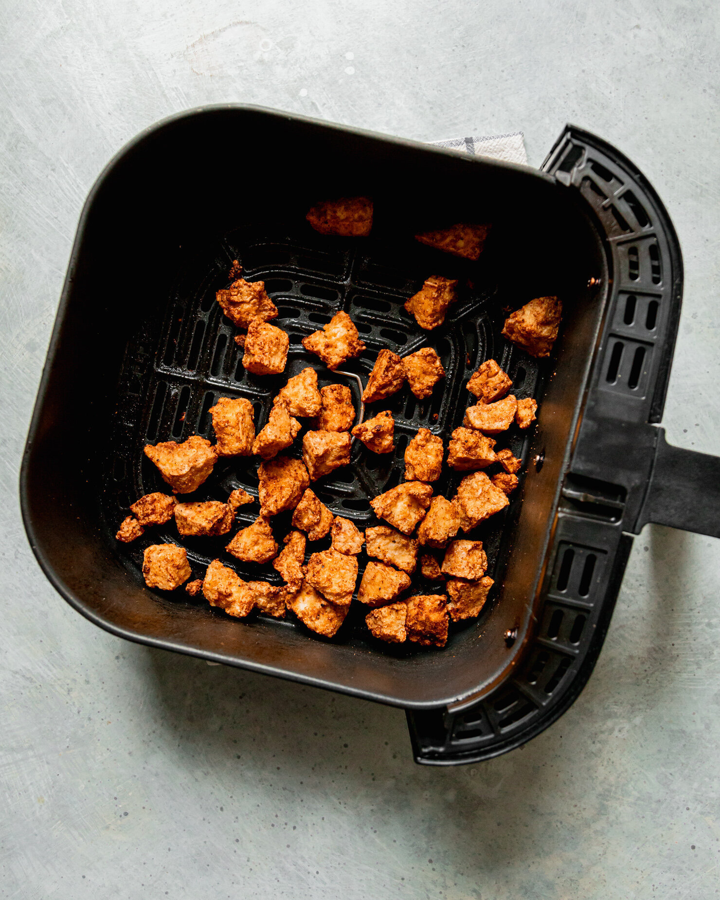 An overhead shot shows a black air fryer basket filled with deeply golden brown torn pieces of crispy tofu.