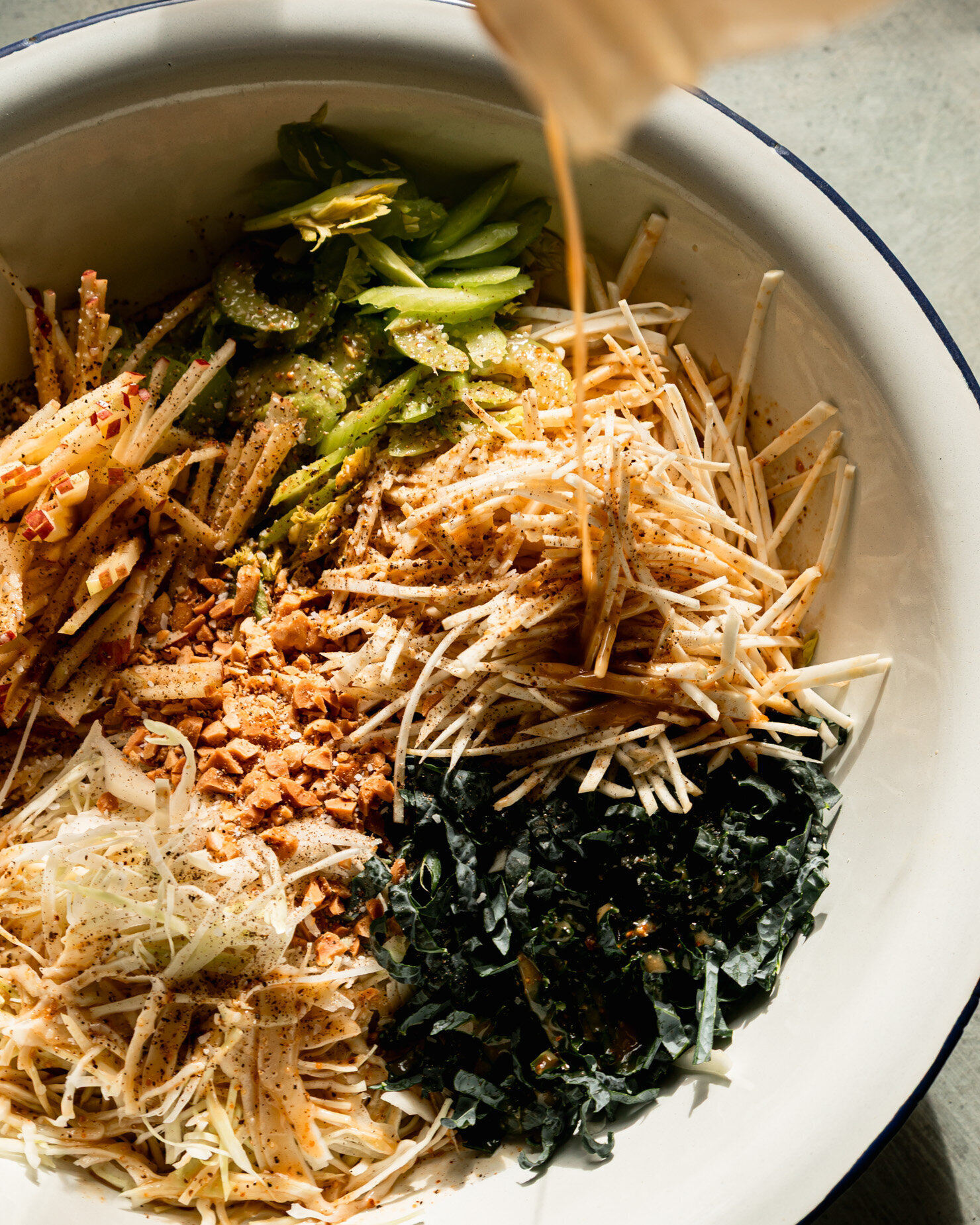 An overhead shot shows maple peanut vinaigrette being poured over julienned vegetables and apple.