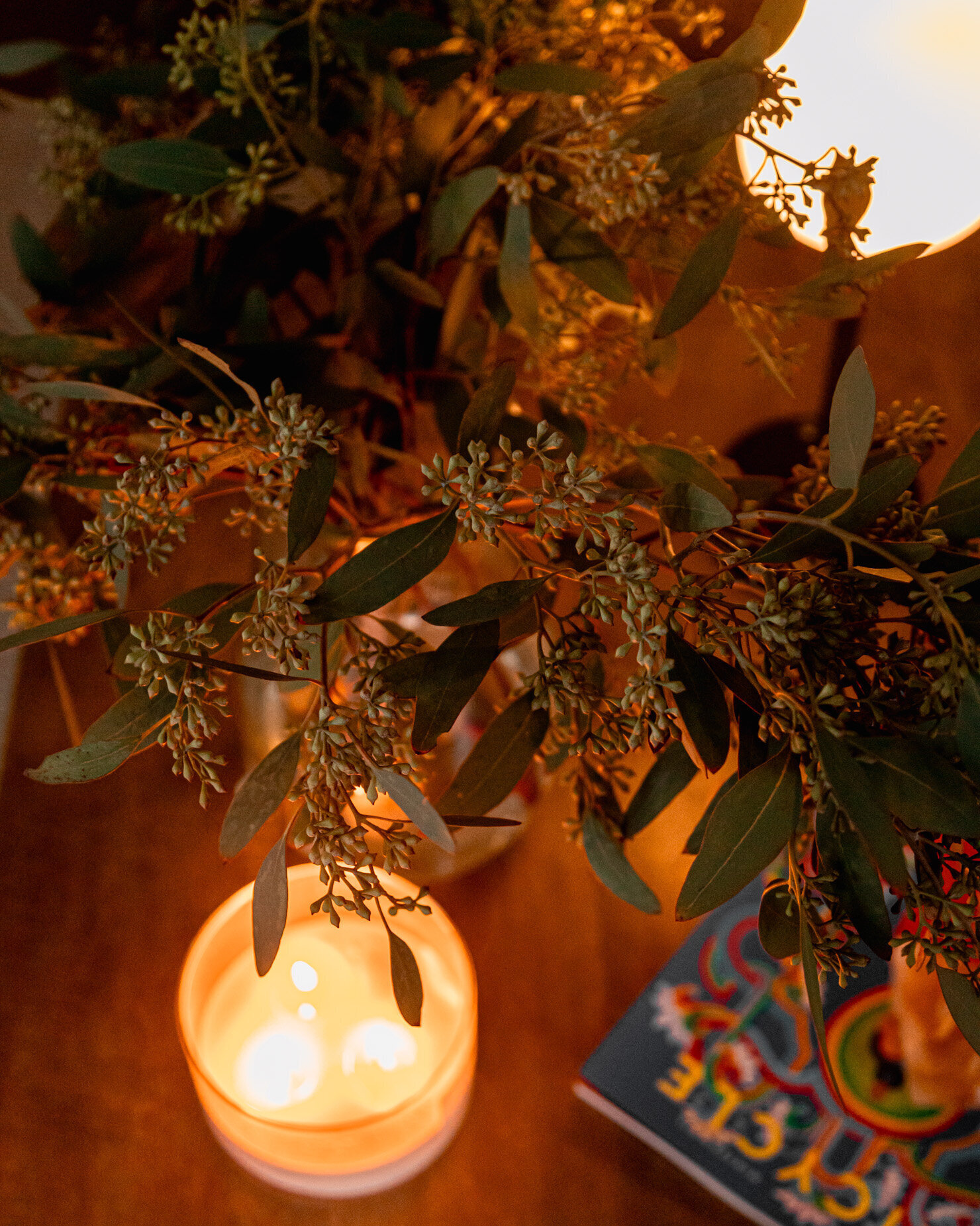 An overhead image shows seeded eucalyptus in a vase. The branches are backlit by glowing candlelight.