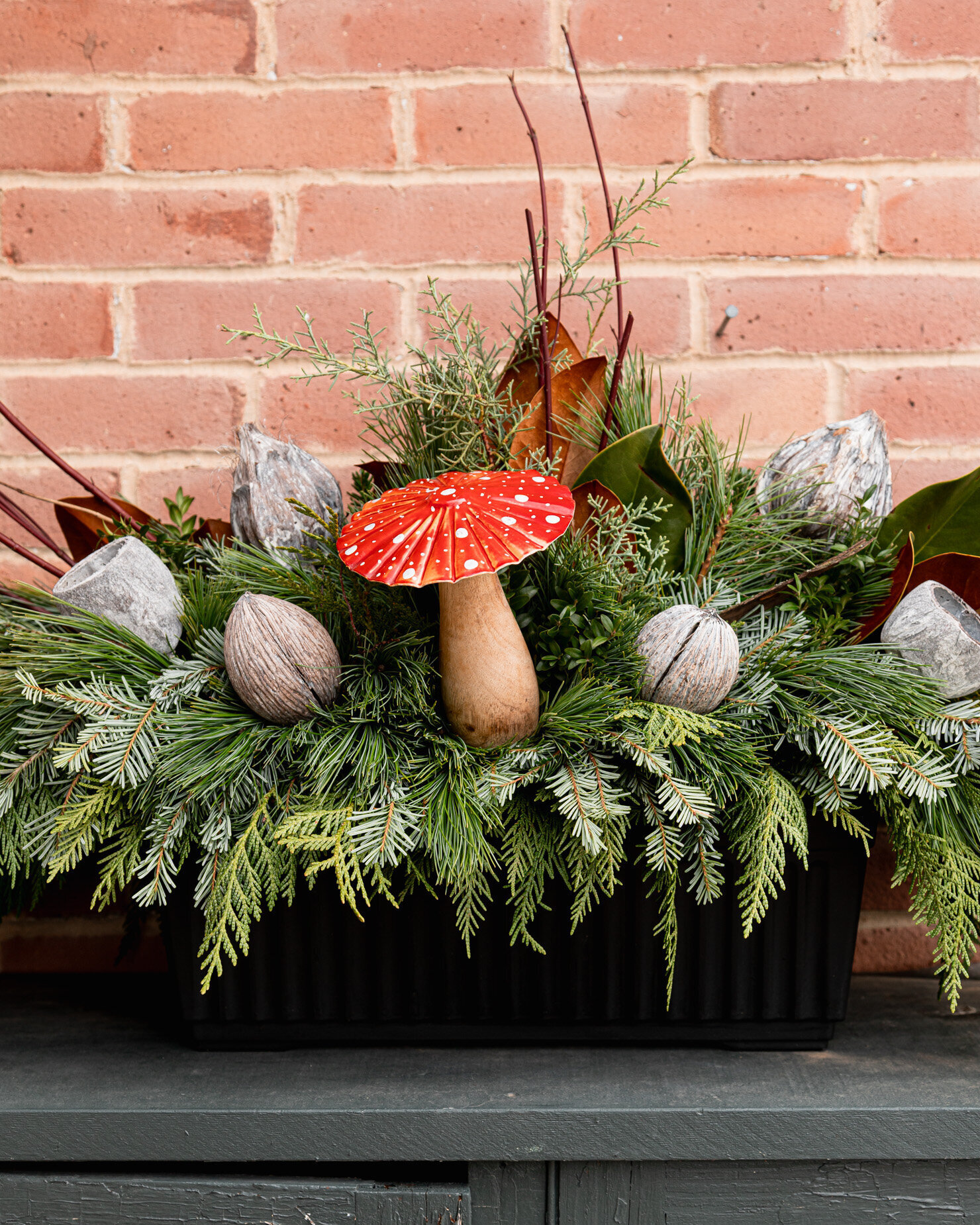 A head-on shot shows a window box filled with winter greens and branches and little holiday ornaments.