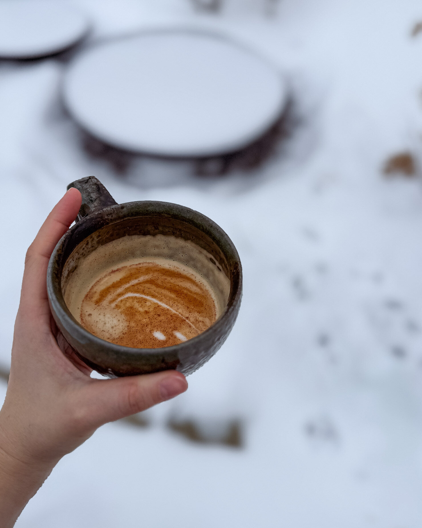 An overhead shot shows a hand holding a half drunk coffee against a backdrop of a snow-covered backyard.