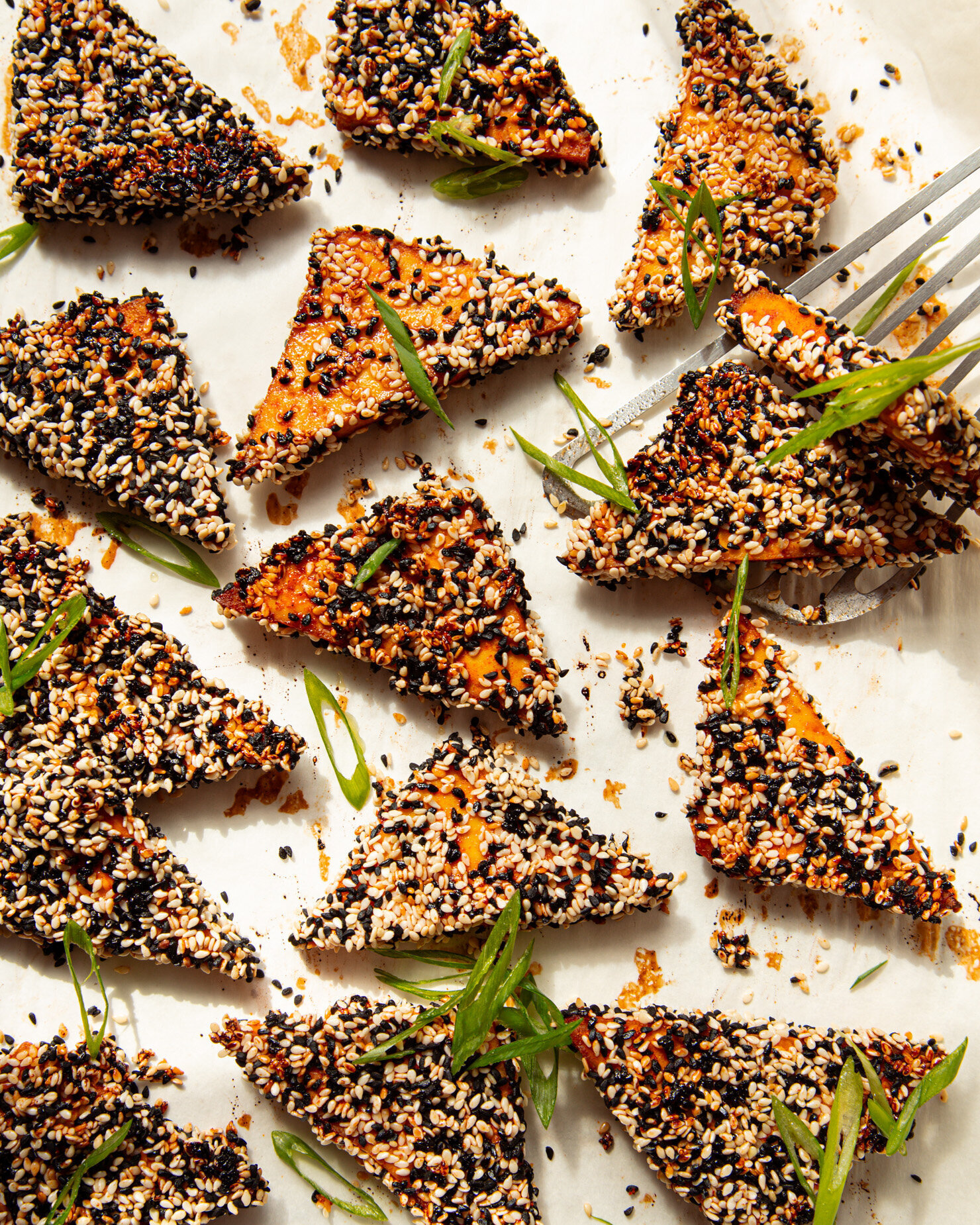An overhead shot shows baked sesame tofu triangles garnished with sliced green onions.