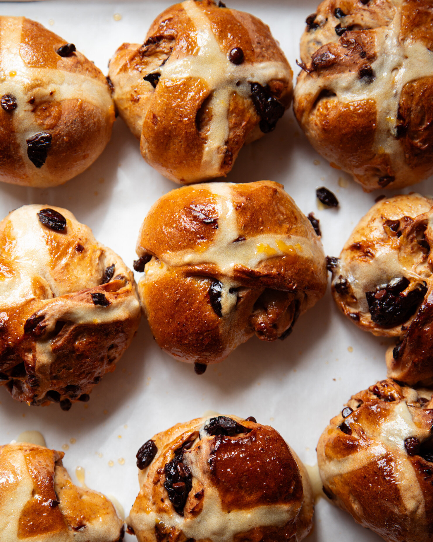 An overhead shot shows freshly baked and glazed vegan hot cross buns with dried cherries and chocolate.